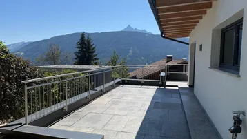 Geräumige geflieste Terrasse mit Metallgeländer und weitem Blick auf die umliegende Berglandschaft.