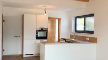 Helle Küche mit weißen Schränken, Holzarbeitsplatte, freiliegenden Holzbalken und Laminatboden.