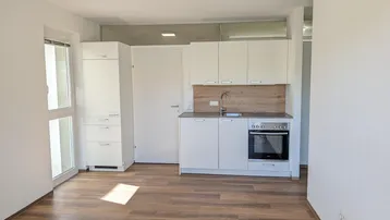 Heller Wohnraum mit integrierter Küchenzeile, Laminatboden und Zugang zum Balkon.
