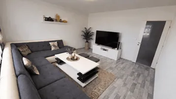 Modernes Wohnzimmer mit großem Ecksofa, TV-Möbel und hellem Laminatboden.