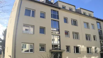 Modernes Mehrfamilienhaus mit heller Fassade, großen Fenstern und gepflegter Grünfläche.