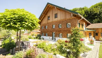 Traditionelles Holzhaus mit gepflegtem Garten und Sitzbereich unter einem Baum an einem sonnigen Tag.