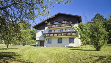 Charmantes Haus mit mehreren Balkonen und großem Garten, umgeben von viel Grün.