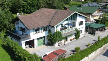 Großzügiges Wohnhaus mit Satteldach, Balkonen und Carport in grüner Umgebung.