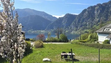 Panoramablick auf den See und die umliegenden Berge mit einem Gartenbereich und Sitzgelegenheiten im Freien.