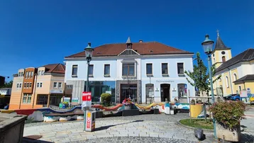 Traditionelles Gebäude mit weißer Fassade und einem Uhrturm im Hintergrund unter strahlend blauem Himmel.