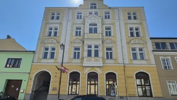 Historisches Gebäude mit gelber Fassade und reich verzierten Fenstern unter strahlendem Sonnenschein.