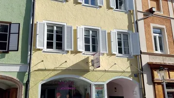 Gelbes Mehrfamilienhaus mit weißen Fensterläden und einem Geschäft im Erdgeschoss an einer Straße.