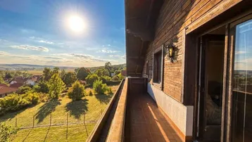 Sonnige Loggia mit Holzbalken und weitem Blick über die grüne Landschaft bei Sonnenuntergang.