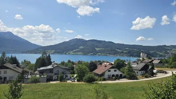 Panoramablick auf einen malerischen See, umgeben von Bergen und einer charmanten Siedlung.