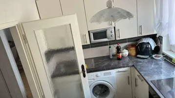 Funktionale Küche mit weißen Hängeschränken, dunkler Arbeitsplatte und integrierter Waschmaschine.