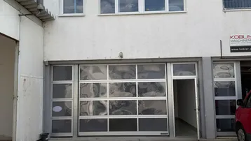 Außenansicht eines Gewerbegebäudes mit großem Garagentor und mehreren Fenstern im Obergeschoss.