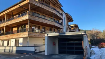 Modernes Gebäude mit Holzfassade, Balkonen und integriertem Carport/Garagenzugang.