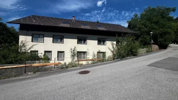 Ansicht des Gebäudes von der Straße aus mit weißer Fassade und Satteldach.
