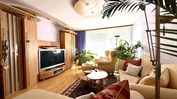 Gemütliches Wohnzimmer mit Holzboden, beigen Sofas und vielen Pflanzen, die eine entspannte Atmosphäre schaffen.