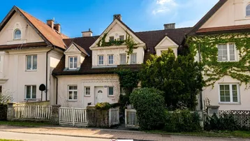 Historische Fassade eines charmanten Hauses mit üppigem Grün und traditionellem Zaun.