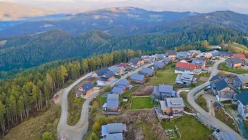 Luftaufnahme eines Bergresorts mit zahlreichen Holzhäusern eingebettet in eine bewaldete Hügellandschaft.