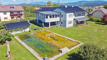 Luftaufnahme des Hauses mit großem Garten, Teich und Bergblick unter blauem Himmel.