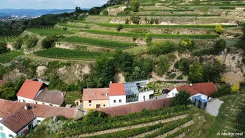Luftaufnahme eines modernen Hauses inmitten von Weinbergen mit traditionellen Gebäuden in der Umgebung.