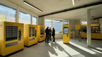 Moderner Innenraum mit gelben Postautomaten, großen Fenstern und Betonoberflächen, ideal für gewerbliche Nutzung.