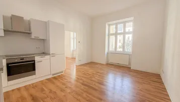 Heller offener Wohnbereich mit integrierter Küchenzeile, Laminatboden und großem Fenster.