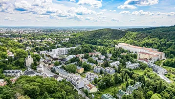 Weitläufige Luftaufnahme der Stadt und der umliegenden grünen Hügellandschaft unter blauem Himmel.