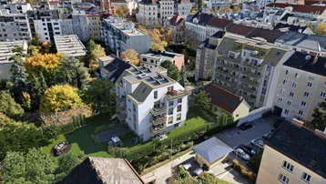 Luftaufnahme eines modernen Wohngebäudes mit Flachdach und Balkonen in einer grünen Stadtlandschaft.
