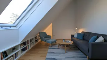 Helles Wohnzimmer im Dachgeschoss mit schräger Decke, Dachfenster und integrierten Bücherregalen.