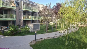 Modernes Mehrfamilienhaus mit Balkonen, begrüntem Gartenbereich, Gehwegen und Photovoltaikanlage auf dem Dach.