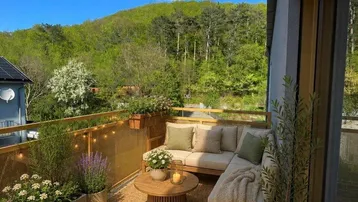 Heller Balkon mit gemütlicher Sitzecke, vielen Pflanzen und weitem Blick ins Grüne.