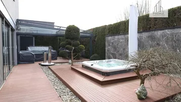 Moderne Terrasse mit integriertem Whirlpool, Holzdeck und überdachtem Sitzbereich, umgeben von einer grünen Hecke.