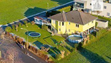 Luftaufnahme eines gelben Einfamilienhauses mit großem Garten, Trampolin und Aufstellpool.