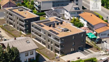 Luftaufnahme von modernen Neubauten mit Flachdächern, Photovoltaikanlagen und Tiefgaragenzufahrt in grüner Umgebung.