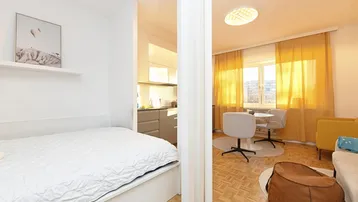 Schlafbereich im Studio-Apartment mit integrierter Küchenzeile und hellem Fensterbereich.