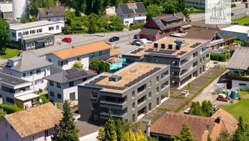 Luftaufnahme einer modernen Wohnanlage mit Photovoltaikanlagen auf den Flachdächern in einer grünen Umgebung.