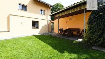Gepflegter Gartenbereich mit Rasenfläche und überdachter Terrasse mit Sitzgelegenheiten am Haus.