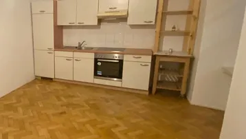 Kleine Einbauküche mit hellem Holzparkett und einfacher Ausstattung, inklusive Backofen.