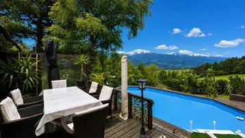 Große Holzterrasse mit Esstisch, Pool und herrlichem Bergblick unter blauem Himmel.