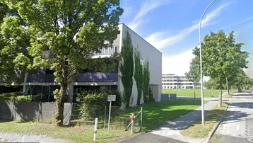 Modernes Mehrfamilienhaus mit schlichter Fassade und begrünten Balkonen an einer Straße.