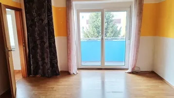 Helles Zimmer mit Parkettboden und Zugang zu einem Balkon, ideal als Wohn- oder Schlafbereich.