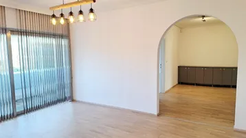 Heller Wohnbereich mit Holzboden, modernen Hängelampen und Zugang zu einem Balkon durch große Fenster.