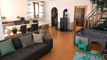 Geräumiger Wohn-Essbereich mit Kaminofen, Holztreppe und Zugang zur Küche, ideal für Familien.