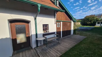 Traditionelles Haus mit Holzterrasse und Gartenbereich unter blauem Himmel.