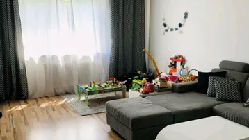 Helles Wohnzimmer mit Holzboden, großem Sofa und viel Tageslicht durch die Fenster.