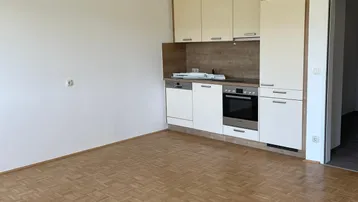 Helle Küchenzeile mit beigen Schränken, integrierten Geräten und Parkettboden in einem Wohnraum.