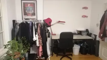 Helles Zimmer mit Schreibtisch, Kleiderstange und Pflanzen, ideal als Arbeits- oder Gästezimmer.