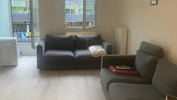Helles Wohnzimmer mit zwei grauen Sofas, hellem Laminatboden und Blick auf die umliegenden Gebäude.
