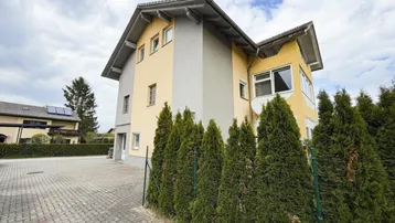 Ansicht des Hauses von der Seite mit gepflasterter Zufahrt und grüner Hecke.