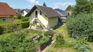 Luftaufnahme eines Einfamilienhauses mit großem Garten und Hochbeeten in ländlicher Umgebung.