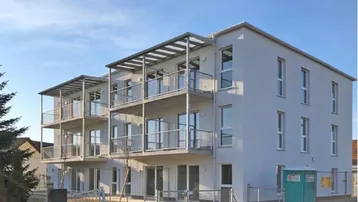 Modernes Mehrfamilienhaus mit mehreren Balkonen und klarer Architektur unter blauem Himmel.